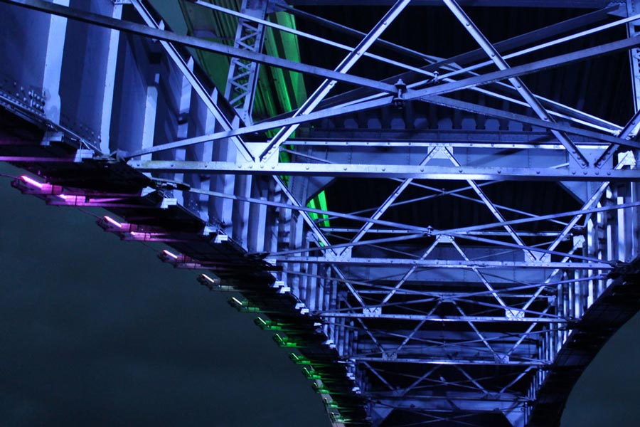 Photo of the underneath of a bridge, lit up in blue lights at night time